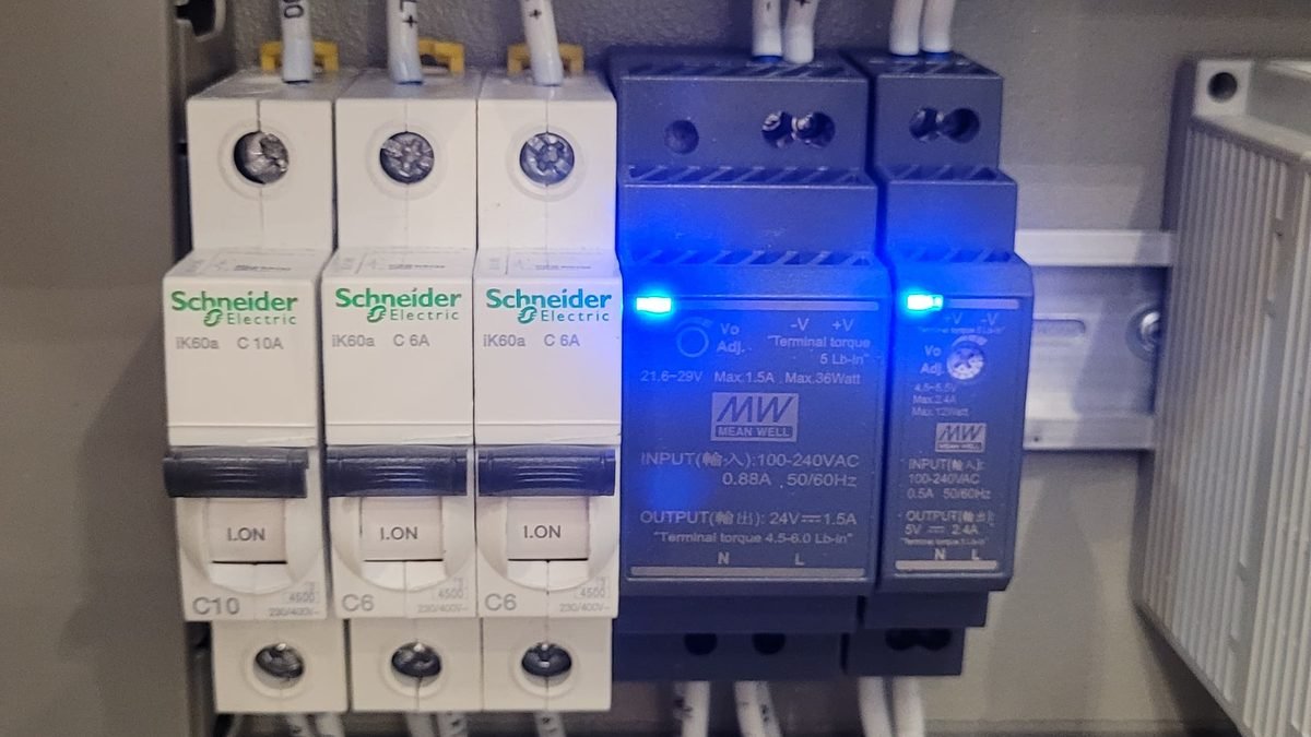 Alimentations Mean Well 24 V et 5 V montées sur rail DIN à côté de disjoncteurs dans une armoire électrique, voyants bleus allumés