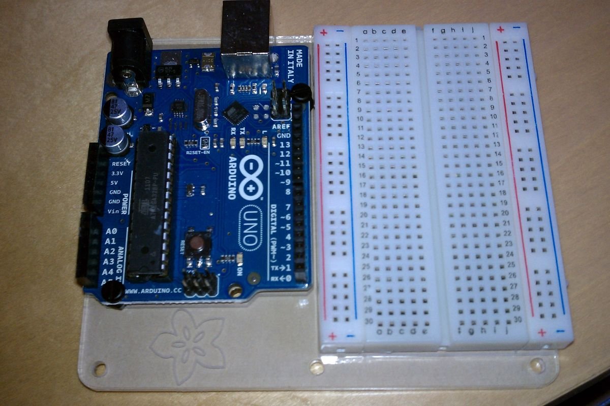 Carte Arduino Uno bleue montée sur un support à côté d’une plaque d’essai blanche sans soudure