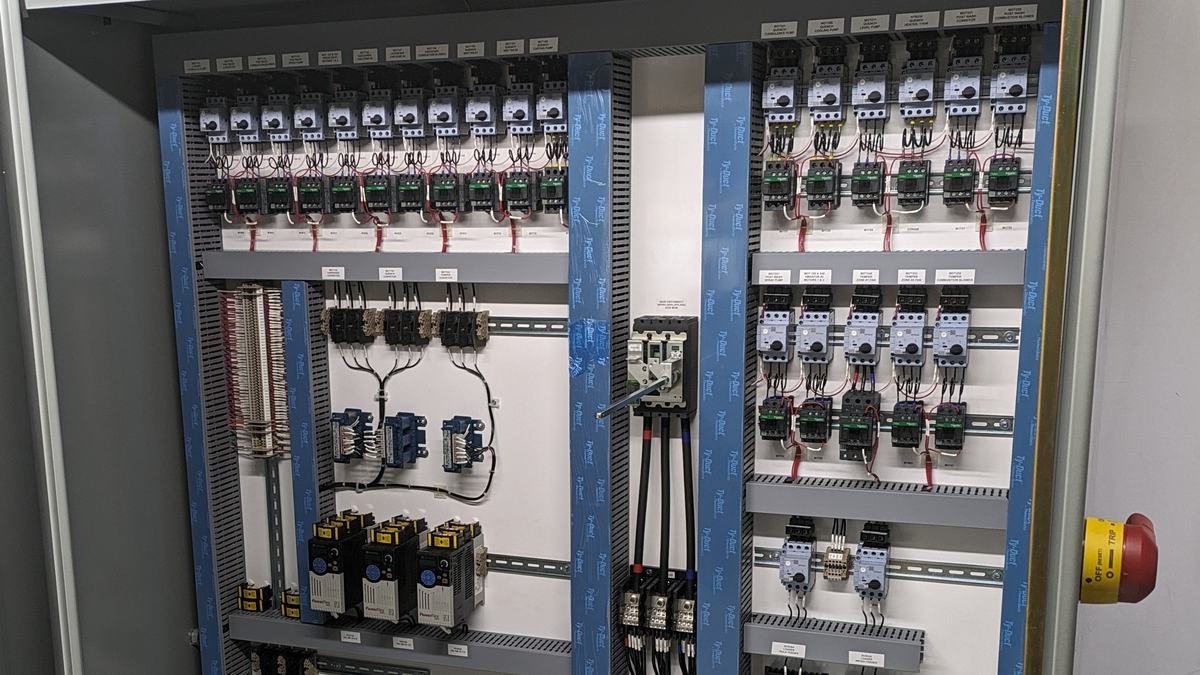 Intérieur d'une armoire électrique bien rangée : rails DIN, disjoncteurs, goulottes bleues et fils repérés par étiquettes