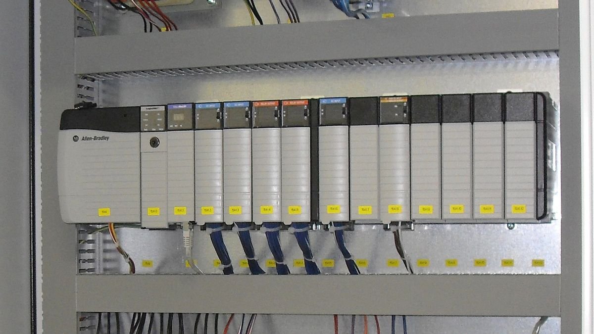 Automate programmable Allen-Bradley avec ses modules d'entrées et de sorties alignés sur un rail dans une armoire électrique, avec goulottes et câbles étiquetés