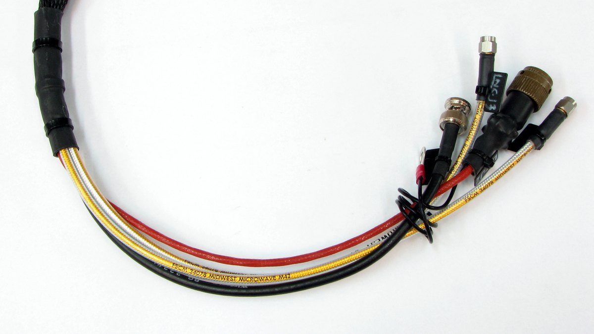 Faisceau de câbles électroniques sous gaine tressée et gaine thermorétractable, terminé par un connecteur circulaire, des connecteurs BNC et SMA, une cosse à œillet et un repère de câble