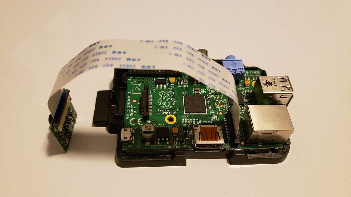 Raspberry Pi dans un boîtier noir relié à un module caméra par un nappe CSI blanche