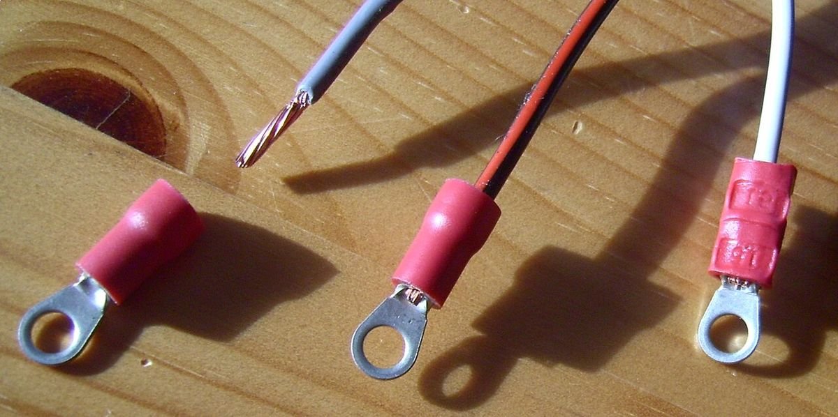 Trois étapes du sertissage : fil dénudé à côté d’une cosse à œillet rouge, fil inséré dans la cosse, puis cosse sertie sur le fil